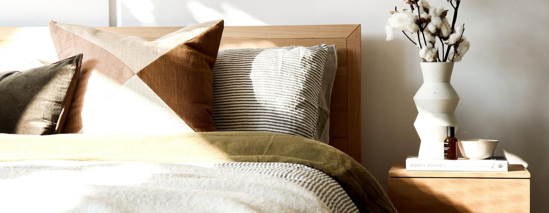 swath of sunlight shines across a well made bed and bedside table with a vase of cotton plants